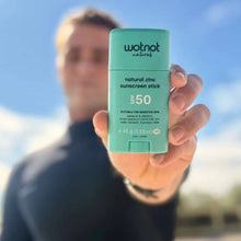 Load image into Gallery viewer, Person holding a Wotnot natural zinc sunscreen stick with a blue sky background