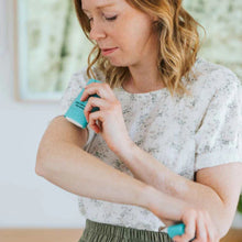 Load image into Gallery viewer, Woman using a blue skin care device on her arm indoors.