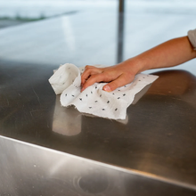 Load image into Gallery viewer, A close-up of a hand wiping a reflective stainless steel surface with a white cloth patterned with small black stars.