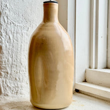Load image into Gallery viewer, A handmade ceramic oil bottle with a glossy beige finish and a metal pour spout, set on a windowsill next to a white textured wall.