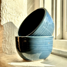 Load image into Gallery viewer, Two blue ceramic bowls stacked on a windowsill with sunlight casting shadows.
