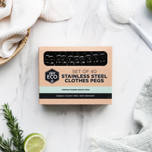Load image into Gallery viewer, A box of WET ECO stainless steel clothes pegs placed on a white marble surface with styled flat-lay props including a towel, spoon, lime, and rosemary.