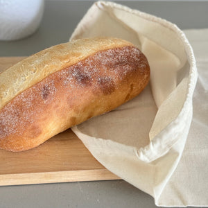 Loaf of bread on a wooden board with a white cloth, against a neutral background.