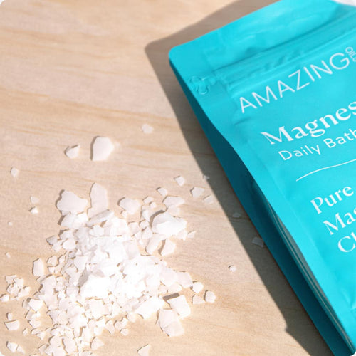 Blue packaging of 'AMAZING' magnesium bath salts on a wooden surface with some of the salt crystals spilling out.