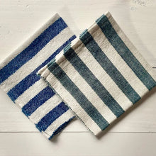 Load image into Gallery viewer, Two striped bath mats, one blue and white, one green and white, on a light wooden floor.
