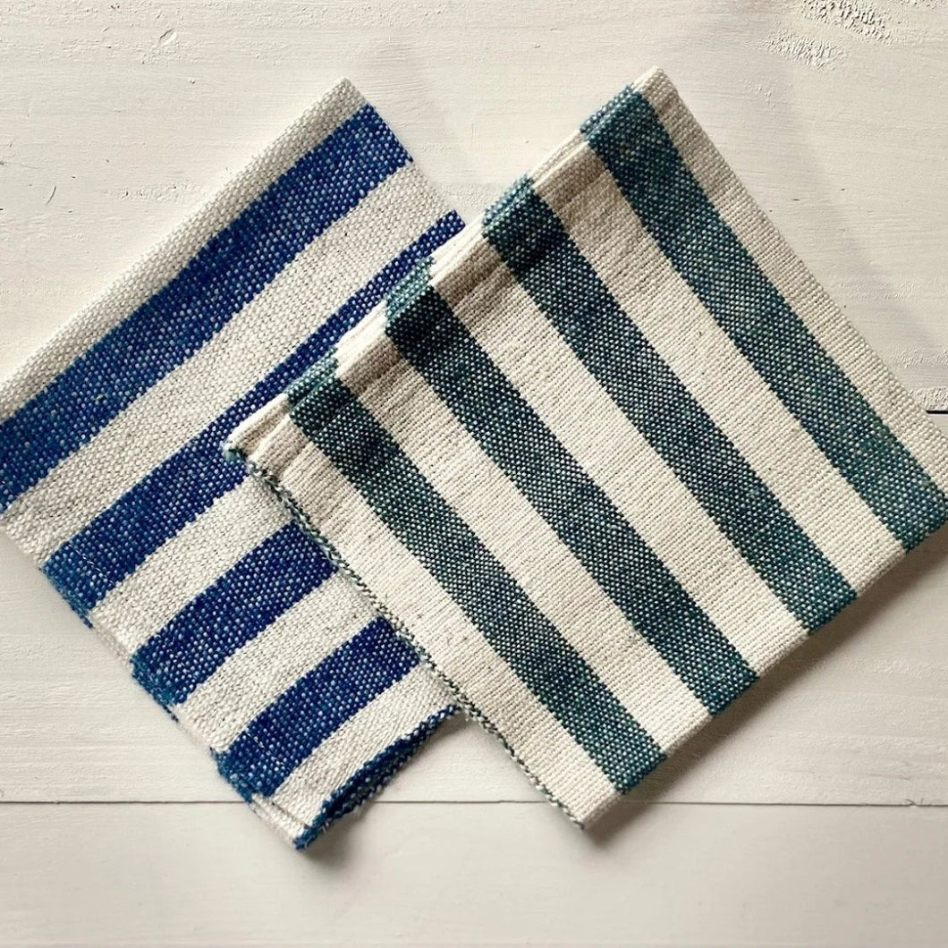 Two striped bath mats, one blue and white, one green and white, on a light wooden floor.
