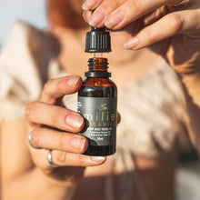 Load image into Gallery viewer, Person holding a bottle of Milie Organics daily facial oil with a blurred background
