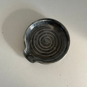 Black ceramic dish with spiral design on a light gray surface