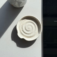Load image into Gallery viewer, Ceramic bowl with spiral design on a light surface next to a speckled ceramic bottle and a black electronic device.
