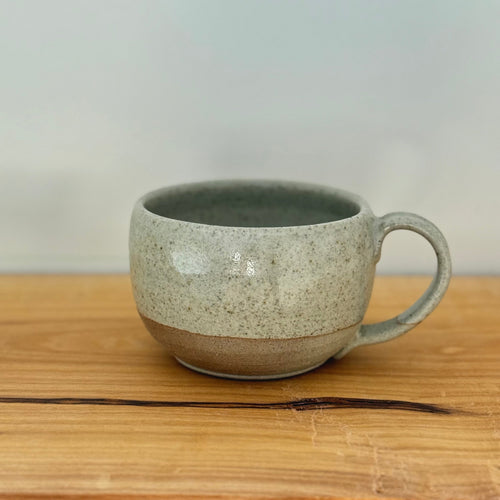 Speckled ceramic mug on a wooden surface with a plain background