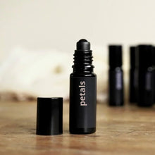 Load image into Gallery viewer, Black rollerball bottle labeled 'petals' on a wooden surface with blurred background
