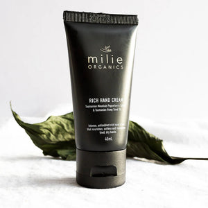 Black tube of milie Organics Rich Hand Cream with green leaves on a light background