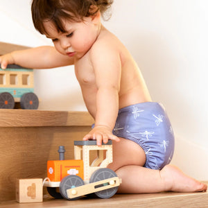 Child playing with wooden toy train wearing a patterned diaper.