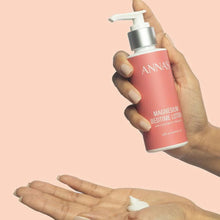 Load image into Gallery viewer, A hand holds a pink pump bottle labeled ANNAS Magnesium Bedtime Lotion above another hand showing a small dollop of white lotion, set against a solid pale peach background.
