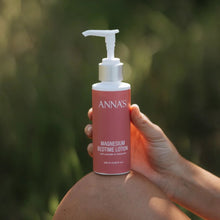 Load image into Gallery viewer, Person holding a bottle of 'ANNAS' magnesium bedtime lotion against a blurred green background
