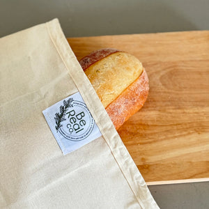 Loaf of bread in a reusable bag with a visible brand label on a wooden surface.