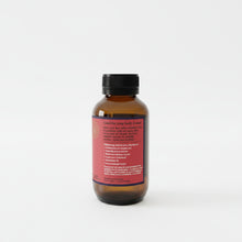 Load image into Gallery viewer, An amber glass bottle of raw hemp seed oil with a black ribbed cap and a red label, photographed on a light gray background.
