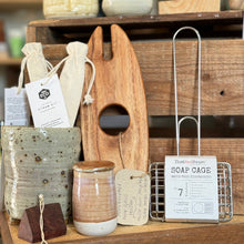 Load image into Gallery viewer, Wooden cutting board, ceramic jars, and soap caddy on a wooden shelf with tags.
