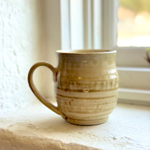 Beige ceramic mug on a windowsill with a blurred window background