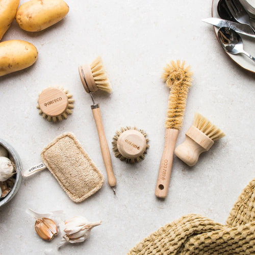 Set of wooden cleaning brushes and sponges on a light surface with garlic and potatoes.