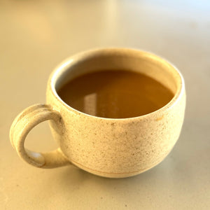 Ceramic mug with a handle filled with a dark liquid on a light surface.