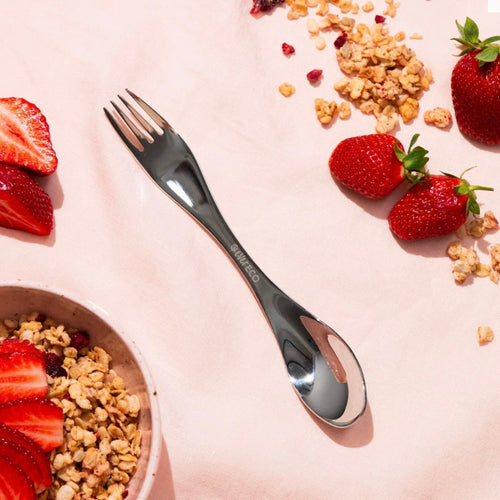 Silver fork on a pink surface with strawberries and cereal