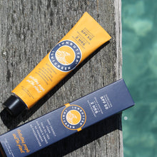 Load image into Gallery viewer, Two tubes of SunBum sunscreen on a wooden post with water in the background
