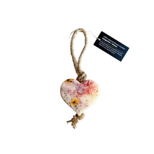 Load image into Gallery viewer, Heart-shaped ceramic ornament with a rope on a textured surface, featuring a label.
